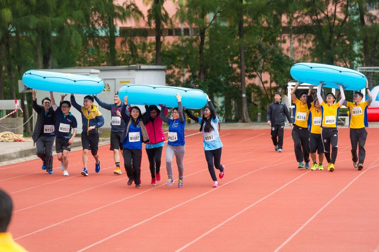 Participants run on a track carrying blue inflatable rafts overhead.